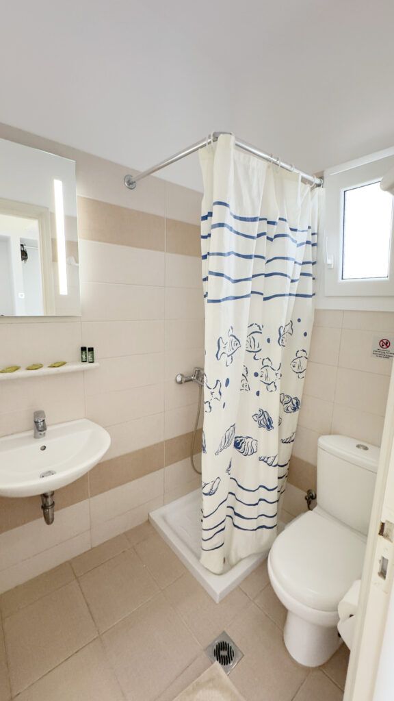 Private bathroom with shower, sink, toilet and illuminated mirror in the Double or Twin Room at Argo Rooms Antiparos.